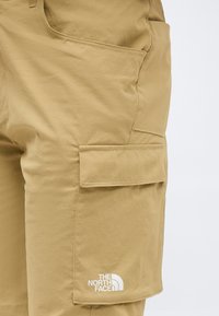 Χακί κοντά παντελόνια cargo με τσέπη με καπάκι και το λογότυπο The North Face στο κάτω μέρος, σε απλό ανοιχτό φόντο.