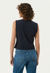 Marineblaue ärmellose Bluse mit taillierter Passform und glatter Textur, kombiniert mit hoch taillierten blauen Jeans aus Denim mit Gesäßtaschen.
