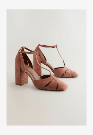 Scarpe con tacco in suede color rosa, con punta chiusa, design a taglio e tacco quadrato spesso. Presentano una cinghia a T e chiusura con fibbia.