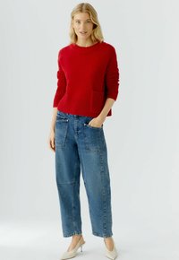 Rode gebreide trui met een ribbelstructuur en een voorzak, gecombineerd met lichtblauwe, hooggesneden denim jeans met grote opgestikte zakken.