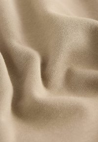 Primo piano di un morbido tessuto beige che mostra una fine trama a maglia e pieghe naturali che creano ombre e luci delicate.