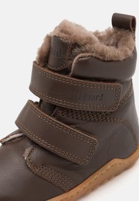 Stivale in pelle marrone con due cinturini a strap in velcro, fodera in pelliccia e suola in gomma texturizzata. Presenta dettagli di cucitura e il marchio sul cinturino.