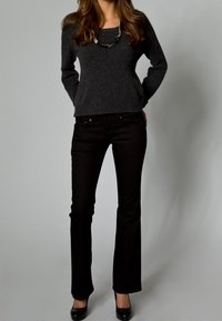 Harmaa pusero pyöreällä pääntiellä, yhdistetty mustiin lievästi levenevälahkeisiin farkkuihin. Mallilla on mustat korkokengät ja helminauha.