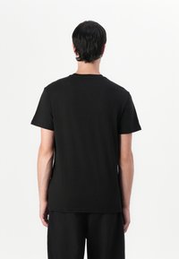 T-shirt en coton noir à manches courtes et col rond, avec un ourlet droit et un design épuré et minimal sans marque visible.