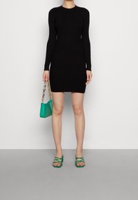 Abito nero a coste con maniche lunghe, dalla forma aderente, abbinato a una borsa verde con texture a coccodrillo e sandali verdi con cinturini.