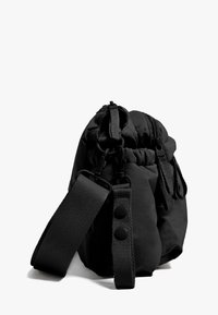 Črna tekstilna torba z nabranim vrhom, nastavljivim trakom in kovinskimi dodatki. Ima gladko teksturo in minimalne detajle.