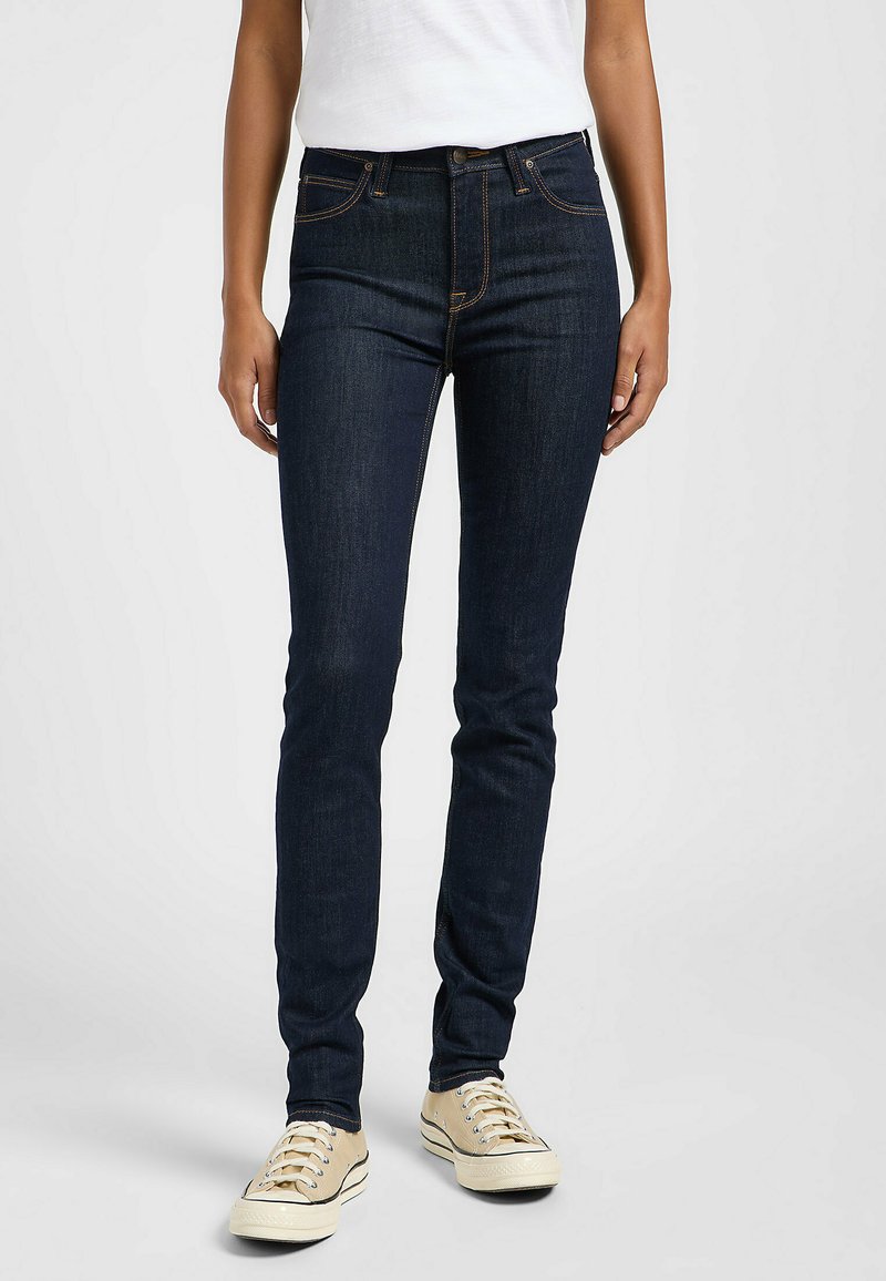 Jeans ajustados en denim azul oscuro. Sus características incluyen una cintura alta, diseño de cinco bolsillos, costuras en contraste y un cierre clásico con botón.