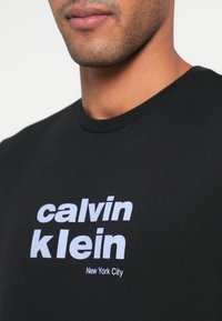 Czarny bawełniany t-shirt z wyrazistym białym napisem "calvin klein" oraz "New York City" w jasnoniebieskim kolorze, okrągły dekolt i krótkie rękawy.