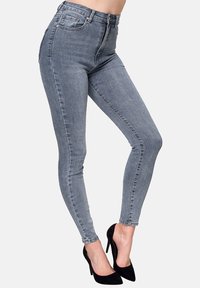 Jeans skinny de tiro alto en gris confeccionados en denim, con costuras visibles, cinco bolsillos, cremallera frontal, y combinados con zapatos de tacón alto negros.