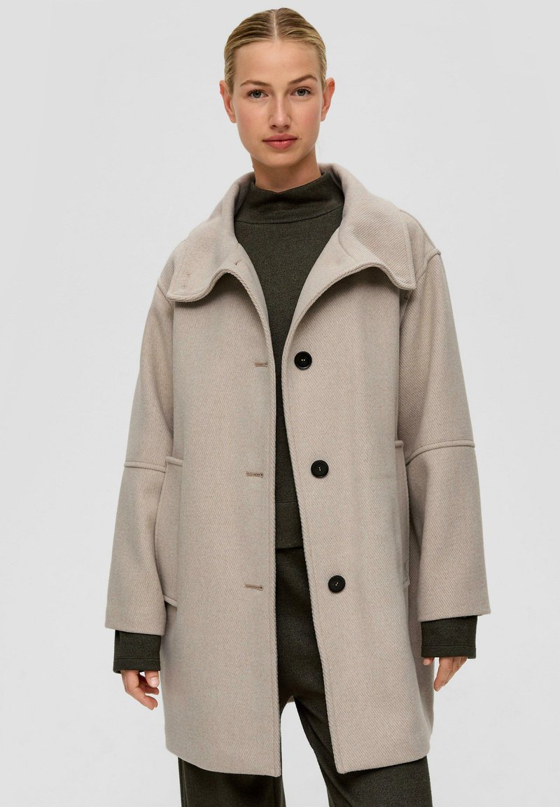 Beige wollen blendjas met een hoge kraag, grote zijzakken, drie knopen en een gestructureerde afwerking. Casual, oversized silhouet.