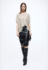 Beige, löst stickad topp med korta ärmar, kombinerad med en figurnära svart läder pennkjol. Svarta knähöga stövlar fullbordar looken.