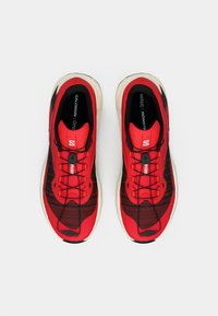 Κόκκινα και μαύρα αθλητικά παπούτσια με πλεκτό επάνω μέρος, υφασμένα κορδόνια και μαλακή σόλα. Διαθέτουν λογότυπο στο πλάι και διακοσμητικά σχέδια.