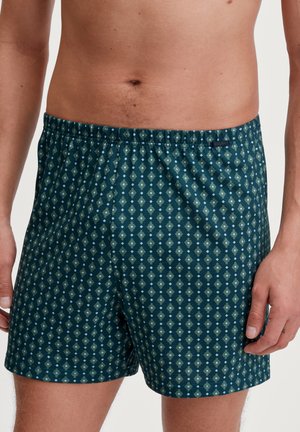 Shorts en coton vert foncé, présentant un motif en losanges vert clair et bleu. Ceinture élastique avec étiquette de marque sur le côté.