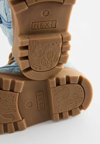 Semelles en caoutchouc de bottes pour enfants avec fer à cheval, empreintes de pattes et logo "NEXT" embossés, taille 6, présentées sur fond blanc.