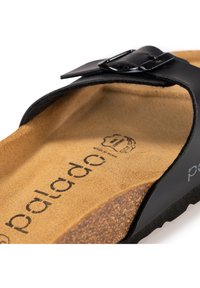 Sandale noire avec une bride présentant une boucle noire brillante. À l'intérieur, il y a un footbed en liège texturé couleur tan avec des détails de logo embossés.