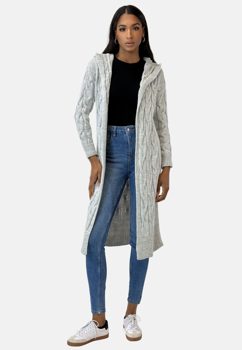Langer grauer Strickcardigan mit Kapuze, strukturiertem Muster, offener Front, kombiniert mit einem schwarzen Oberteil und blauen Jeans, getragen mit weißen Sneakers.