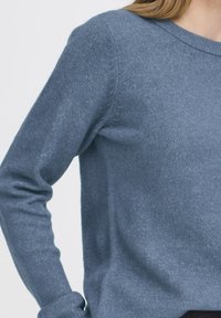 Sinine villane kampsun ümmarguse kaelusega, pikad varrukad ja pehme tekstuuriga. Omab vormi järgivat disaini ja soonikkoes mansette.