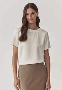 Bílá blůza s krátkým rukávem a kulatým výstřihem, hladkého materiálu, v kombinaci s padnoucí hnědou sukní. Jednoduchý, čistý design.