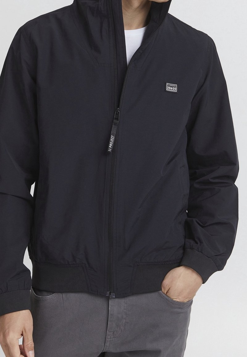 Giacca bomber nera con zip, con polsini e orlo a coste, caratterizzata da una piccola etichetta con logo, realizzata in un tessuto leggero e liscio.