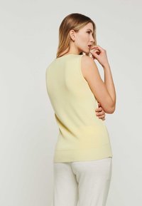 Helles gelbes ärmelloses Stricktop mit figurschmeichelndem Design, geripptem Saum und glatter Textur, kombiniert mit kremfarbenen Hosen.