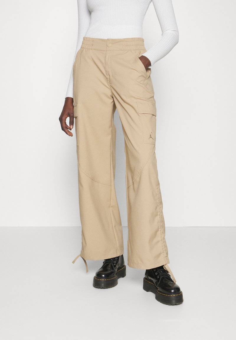 Pantaloni cargo beige con vestibilità comoda, molteplici tasche laterali e waistband elasticizzato. Indossati con stivali platform neri. Tessuto liscio e resistente.