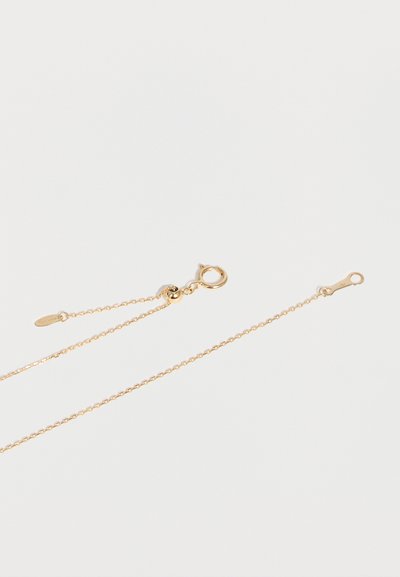 Collier délicat en chaîne d'or avec un fermoir rond à ressort et une petite étiquette attachée près du fermoir sur un fond blanc uni.