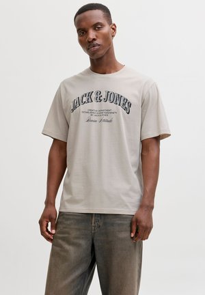 Jasnoszara koszulka wykonana z bawełny, z granatowym napisem "JACK & JONES" w zakrzywionym układzie, z krótkimi rękawami i luźnym krojem.