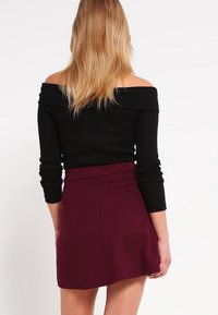 Czarny prążkowany top typu off-the-shoulder z długimi rękawami, zestawiony z bordową mini spódnicą z dopasowanym stanem i subtelnym detalem szwów.