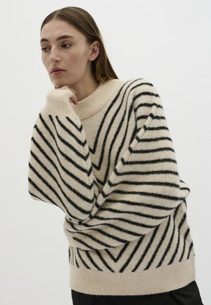 Oversized sweater in cream with black vertical stripes, featuring a ribbed neckline and textured fabric for warmth and comfort.