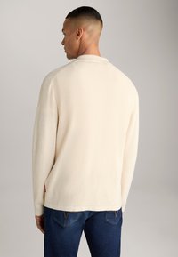 Maglione a maglia color crema con superficie testurizzata, maniche lunghe e colletto. Abbinato a jeans in denim blu scuro.