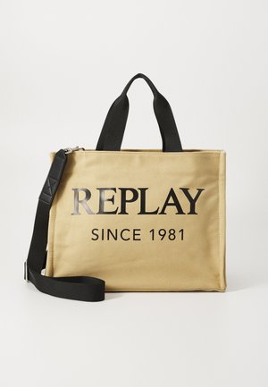 Bolsa de lona amarilla con asas negras y correa ajustable. Presenta una impresión en negrita de color negro "REPLAY DESDE 1981" en el frente. Textura suave.
