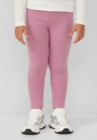 Rosa Leggings aus dehnbarem Material, enganliegendes Design mit glatter Textur. Kombiniert mit weißen Sneakern mit silbernen Akzenten.