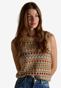 Kootud varrukateta sviiter beeži värviga, millel on mitmevärvilised lille- ja geomeetrilised musterid. Koos teksadega, millel on nupuga sulgemine.