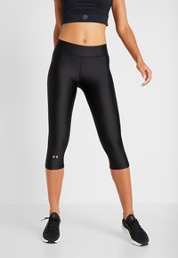 Czarne legginsy capri z gładkiego, elastycznego materiału. Posiadają wysoki stan i detal z logo blisko dolnej krawędzi. Idealne do użytku sportowego.