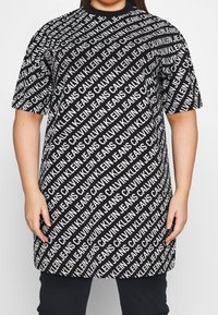 Svart oversize T-shirt med ett upprepat vitt textmönster av "CALVIN KLEIN JEANS." Korta ärmar och rund halsringning.