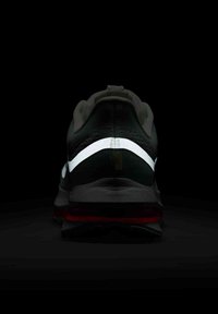 Black athletic shoe featuring a textured upper, reflective midsole stripe, and red accents on the sole, viewed from the rear.