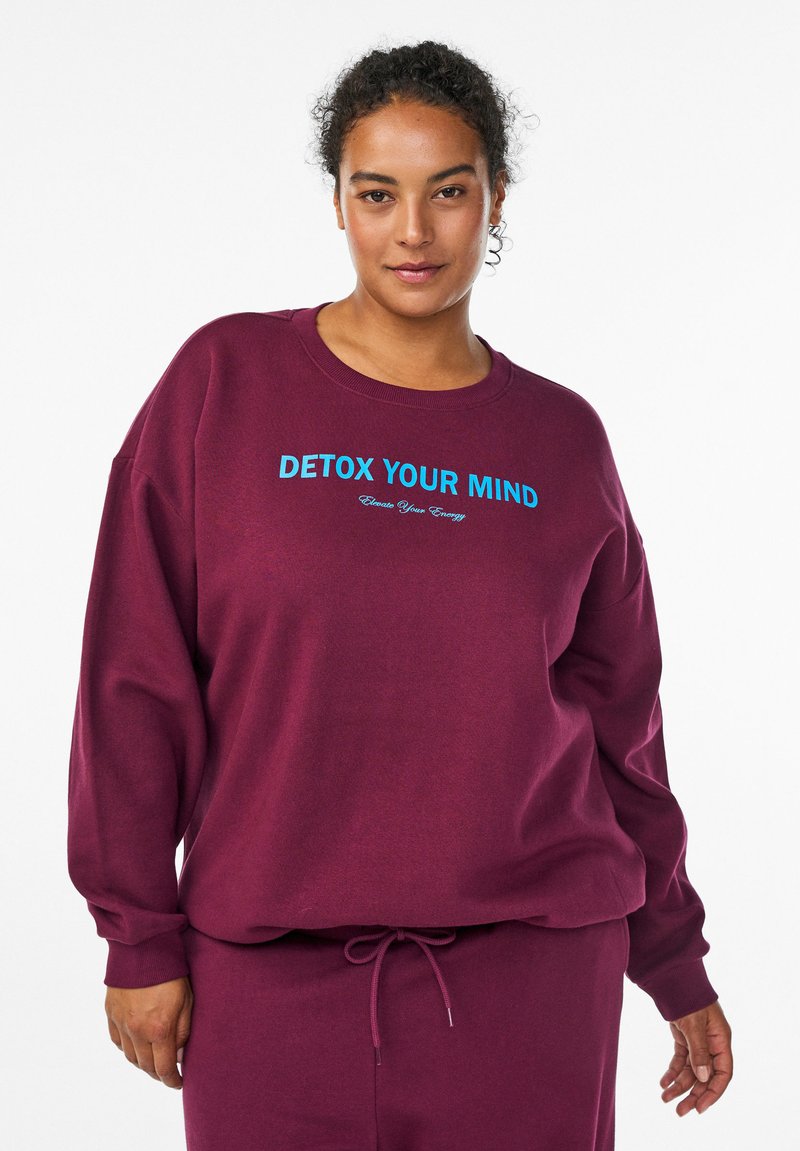 Bordová mikina z mäkkej látky s voľným strihom. Má modrý nápis "DETOX YOUR MIND" a "Create Your Energy." Sťahovacia šnúrka v oblasti pásu.