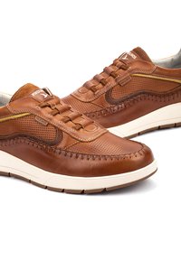 Baskets en cuir marron avec un design perforé et des coutures contrastées. Elles présentent une semelle en caoutchouc beige et une fermeture à lacets marron.