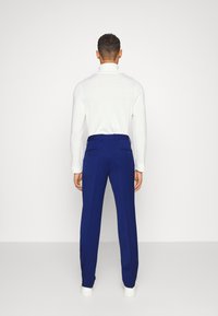 Blaue Maßhose mit glatter Textur, im Slim-Fit-Schnitt und mit Gesäßtaschen, kombiniert mit einem weißen Langarmoberteil.