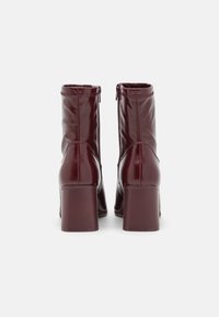 Bottines synthétiques bordeaux à finition brillante, talons carrés, fermeture éclair à l'arrière, avec des détails de coutures sur les côtés.