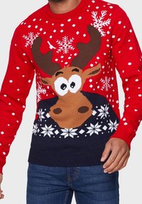 Czerwony sweter z dzianiny z nadrukiem kartonowego renifera z dużymi oczami, płatkami śniegu oraz granatową dolną częścią. Noszony przez osobę.