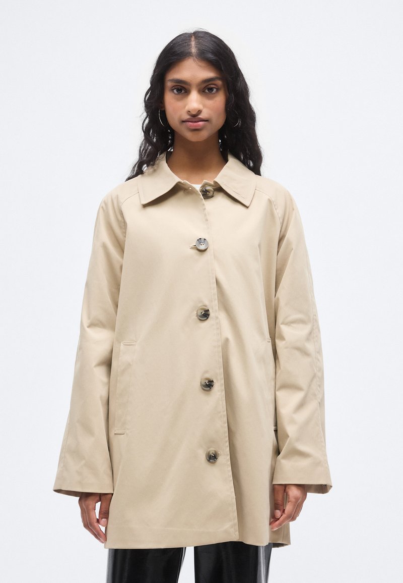 Μπεζ ελαφρύ παλτό με γιακά, μπροστινά κουμπιά και πλαϊνές τσέπες. Διαθέτει φαρδιά μανίκια και λεία υφή.