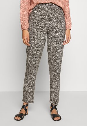 Czarno-białe spodnie z wzorem, o luźnym kroju, z elastycznym pasem i kontrastującymi sandałami na neutralnym tle.