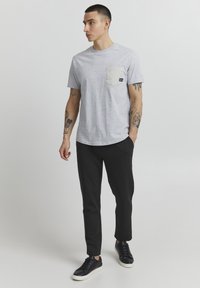 Gray short-sleeve t-shirt with a chest pocket in beige, paired with dark gray pants and black sneakers, featuring a minimalistic design.