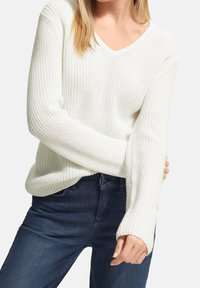 Biały sweter robiony na drutach z dekoltem w kształcie litery V, prążkowaną teksturą i długimi rękawami; w połączeniu z ciemnoniebieskimi dżinsami. Przytulny i swobodny design.
