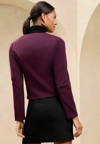 Mustra turtleneck mustriga mustleitse all sügavas burgundihalli sobitatud lühikese jope all; sile kangas struktuurse silueti ja pikkade varrukatega.