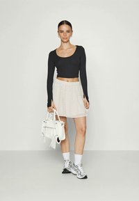 Juoda ilgomis rankovėmis crop top tipo palaidinė, šviesiai rožinė pūsta sijonas su zigzago raštu, balta rankinė, pilki sportbačiai, baltos kulkšnies kojinės.