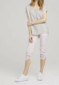 Lekka, krótki rękaw, jasna bluzka z kluczowym detalem z przodu; zestawiona z spodniami w pastelowym różu z podwiniętymi mankietami i białymi sneakersami.