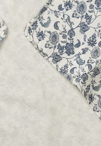 Kukkakuosisissa kankaissa on sinisiä kukkia vaalean kerma-taustalla, ja ne on yhdistetty pehmeään, teksturoituun valkoiseen kankaaseen. Kuosisessa on kukkia ja pieniä eläimiä.