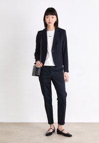 Granatowa marynarka na białej koszulce z napisem "BOSS", zestawiona z czarnymi spodniami i czarnymi płaskimi butami, noszona z małą czarną torebką.